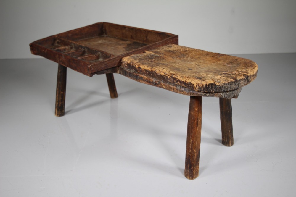 A 19th-century English wooden cobblers bench featuring a flat seating area on one side and a partitioned tray with tool compartments on splayed wooden legs. View VI