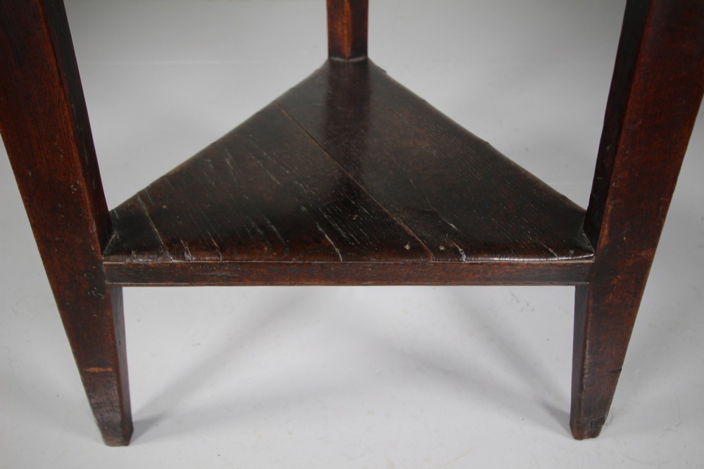 An 18th-century English oak cricket table featuring a circular top, three tapered legs, and a lower triangular shelf. View III