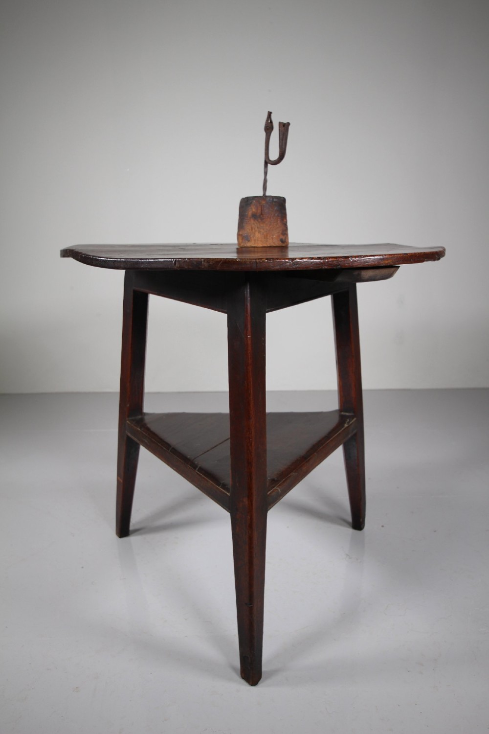 An 18th-century English oak cricket table featuring a circular top, three tapered legs, and a lower triangular shelf. View VI