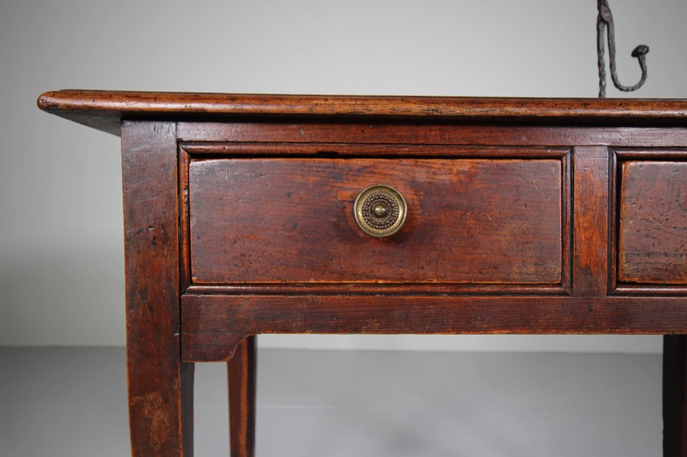 An 18th-century English side table crafted from warm brown elm and fruitwood featuring two drawers with circular brass drop handles and tapered legs. View II