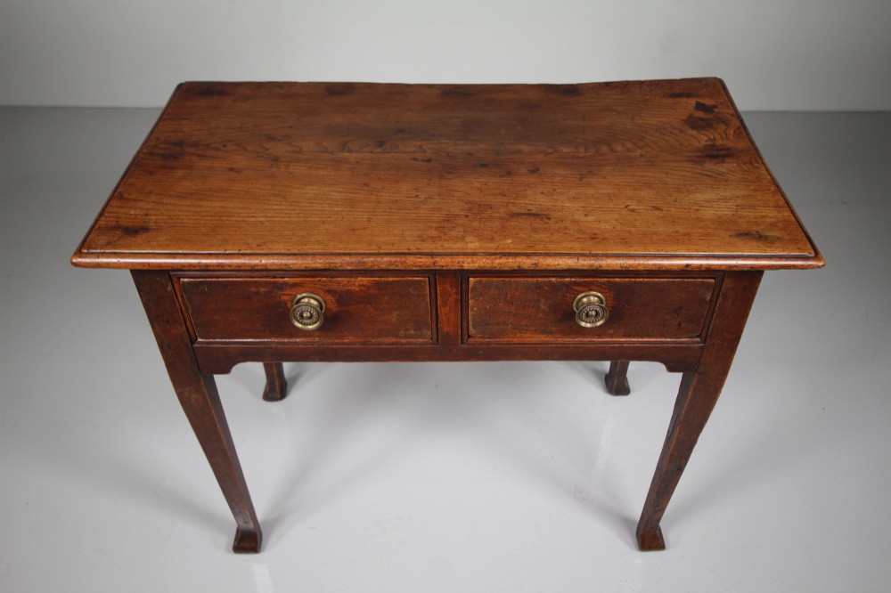 An 18th-century English side table crafted from warm brown elm and fruitwood featuring two drawers with circular brass drop handles and tapered legs. View V