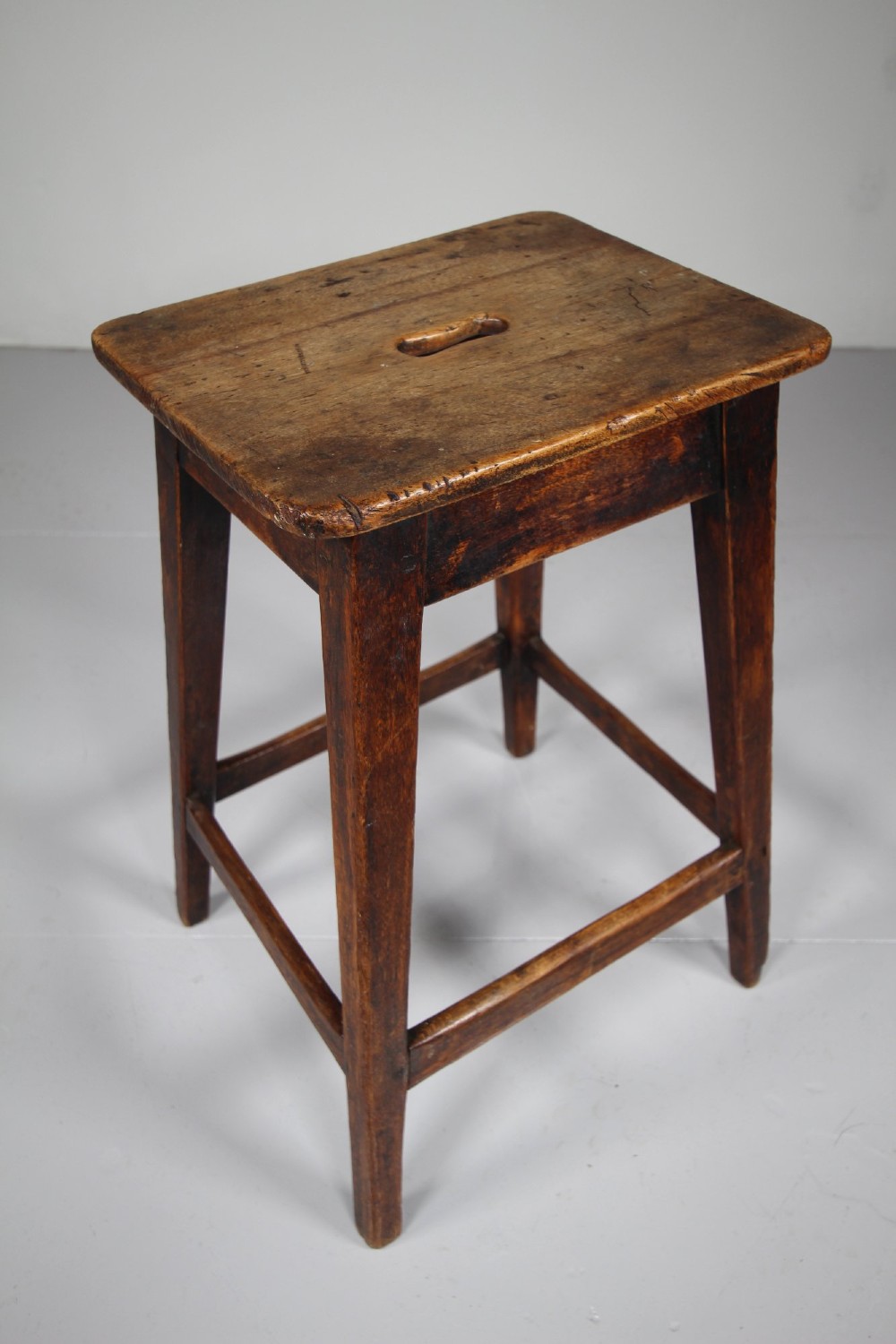 A dark brown antique wooden tall stool with a square seat, four tapered legs, and four horizontal stretchers. View II