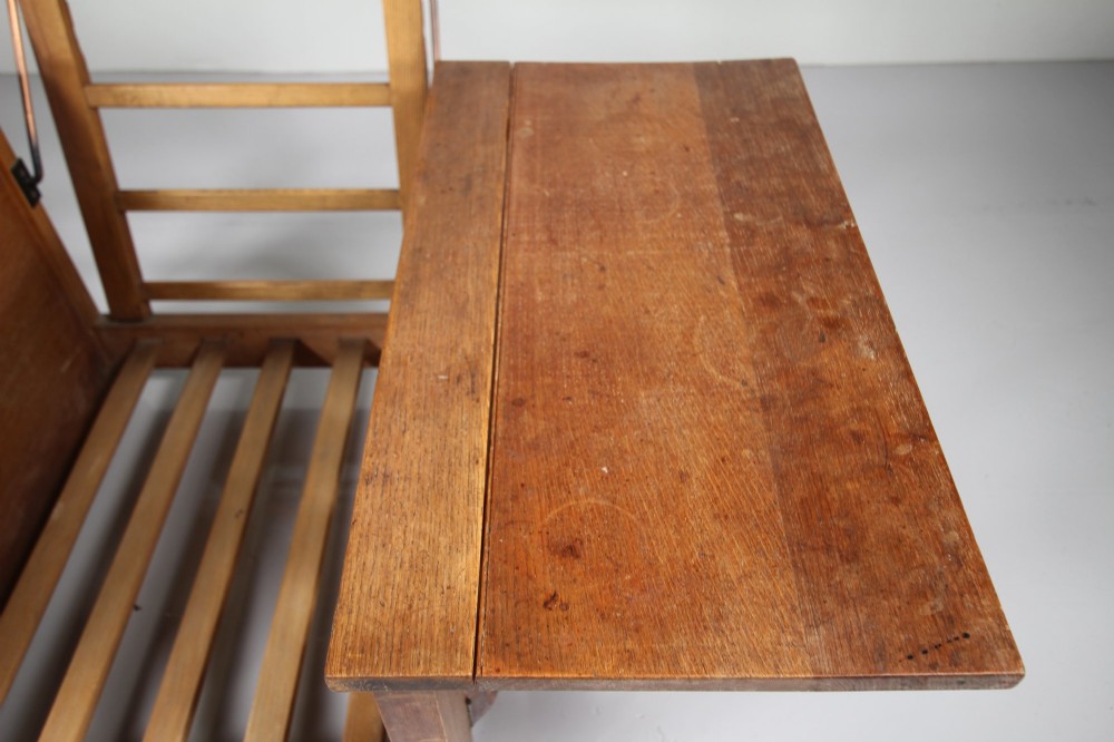 A 1930s solid oak reclining armchair frame featuring integrated side bookshelves, an adjustable slatted backrest, and a folding drop-leaf side table. View II