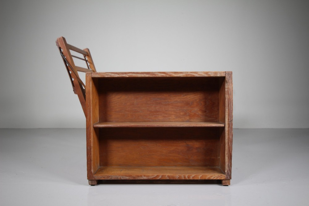 A 1930s solid oak reclining armchair frame featuring integrated side bookshelves, an adjustable slatted backrest, and a folding drop-leaf side table. View IV