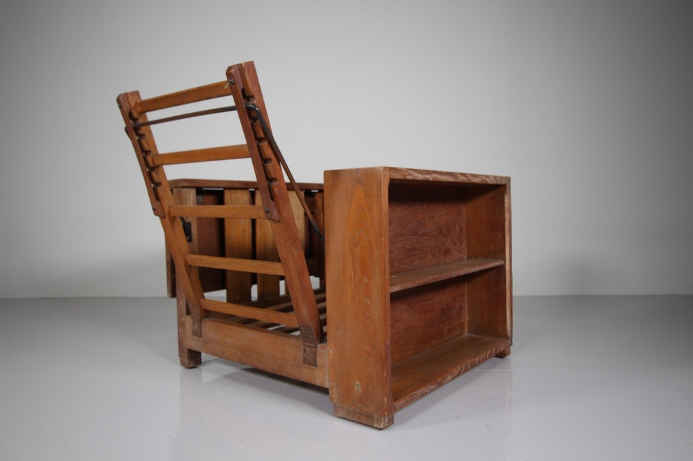 A 1930s solid oak reclining armchair frame featuring integrated side bookshelves, an adjustable slatted backrest, and a folding drop-leaf side table. View V
