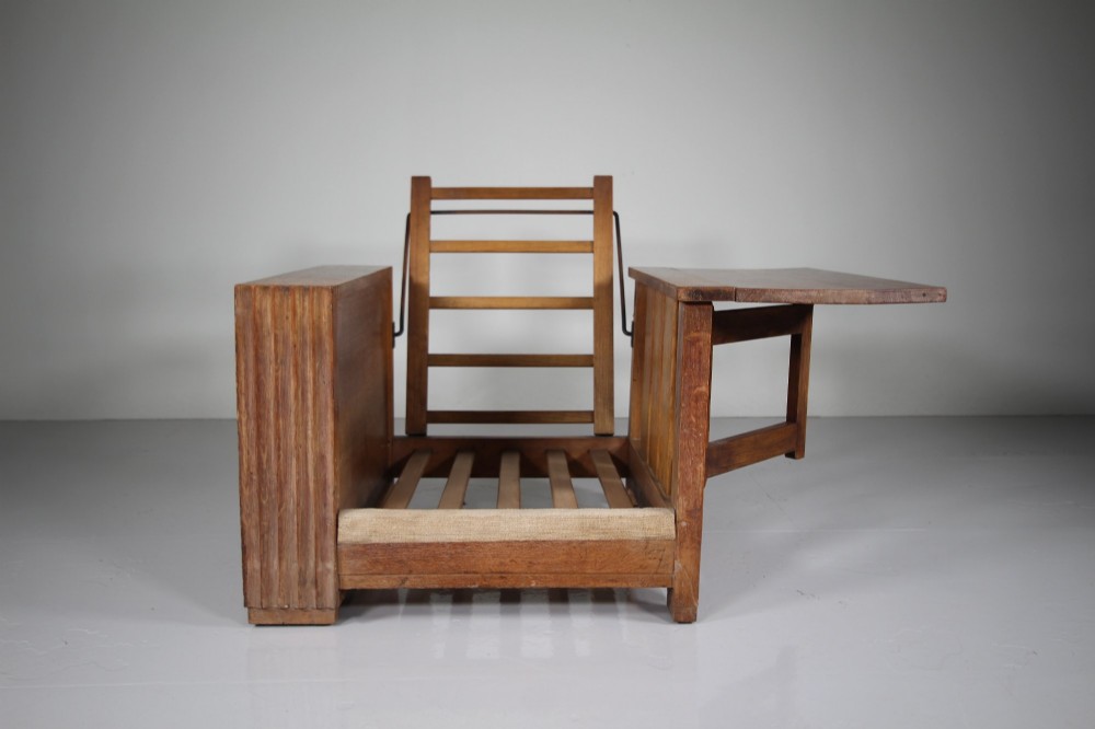 A 1930s solid oak reclining armchair frame featuring integrated side bookshelves, an adjustable slatted backrest, and a folding drop-leaf side table. View VIII