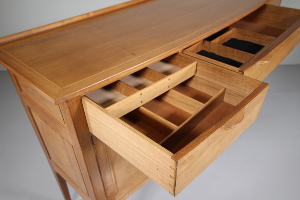 A pale walnut sideboard featuring four drawers above four cabinet doors with panelled detailing and tapered legs. View II