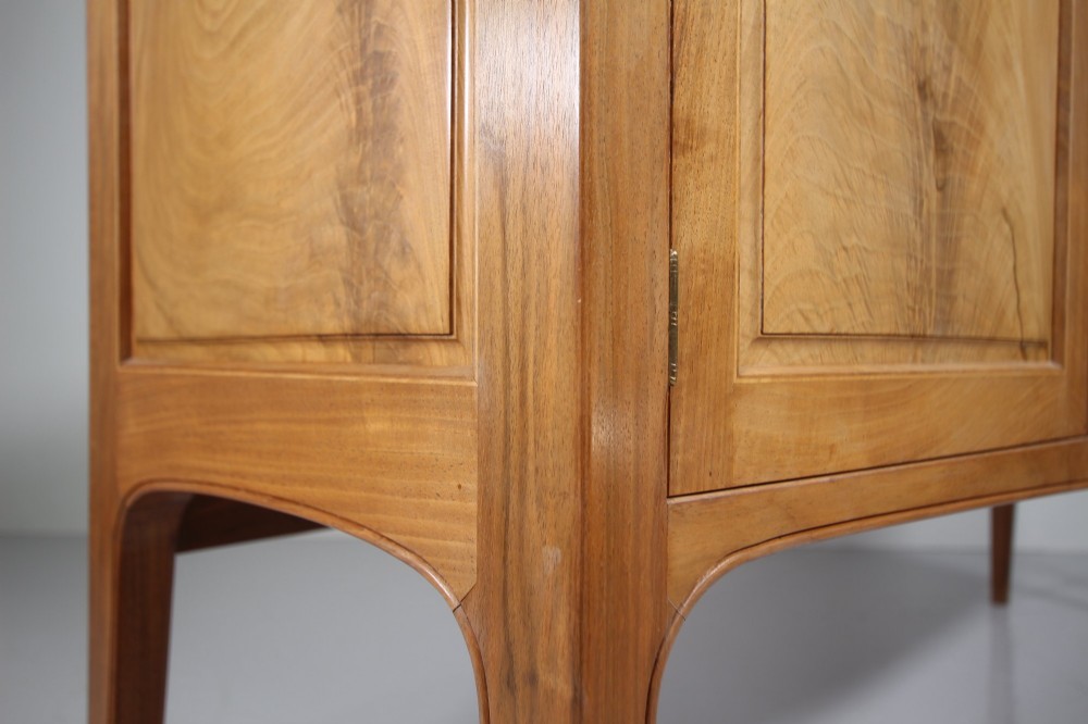 A pale walnut sideboard featuring four drawers above four cabinet doors with panelled detailing and tapered legs. View V