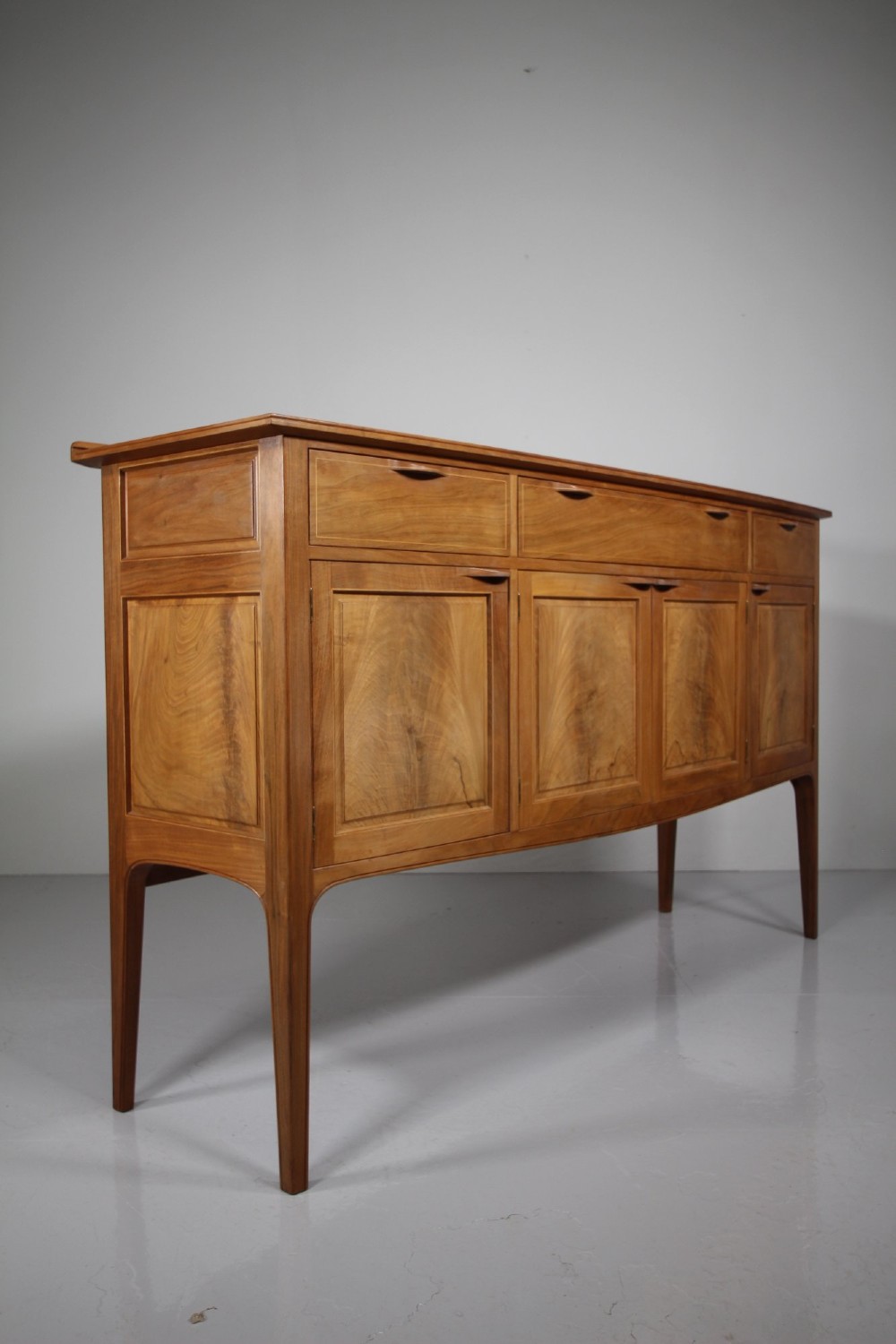 A pale walnut sideboard featuring four drawers above four cabinet doors with panelled detailing and tapered legs. View VI