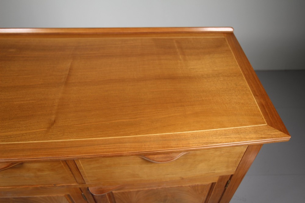 A pale walnut sideboard featuring four drawers above four cabinet doors with panelled detailing and tapered legs. View XII