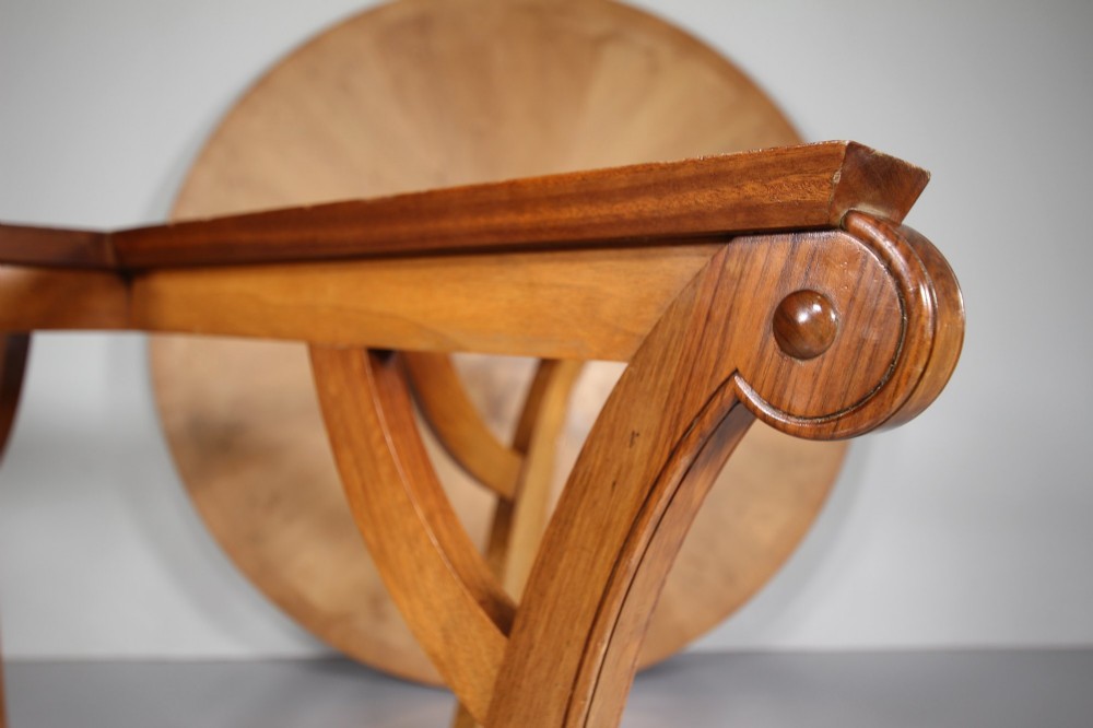 An English Art Deco circular dining table crafted from light timber with a veneered top supported by a curved four-leg pedestal base and cross stretcher. View II