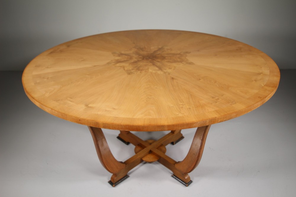 An English Art Deco circular dining table crafted from light timber with a veneered top supported by a curved four-leg pedestal base and cross stretcher. View V