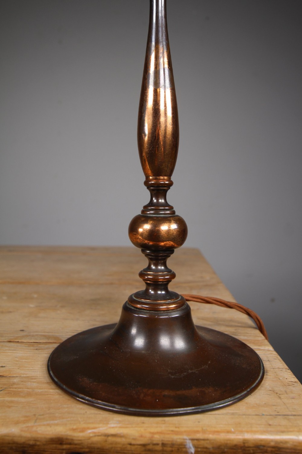 An antique coppered metal table lamp base featuring a turned baluster stem, a stepped circular foot, and a brass bulb fitting. View IV