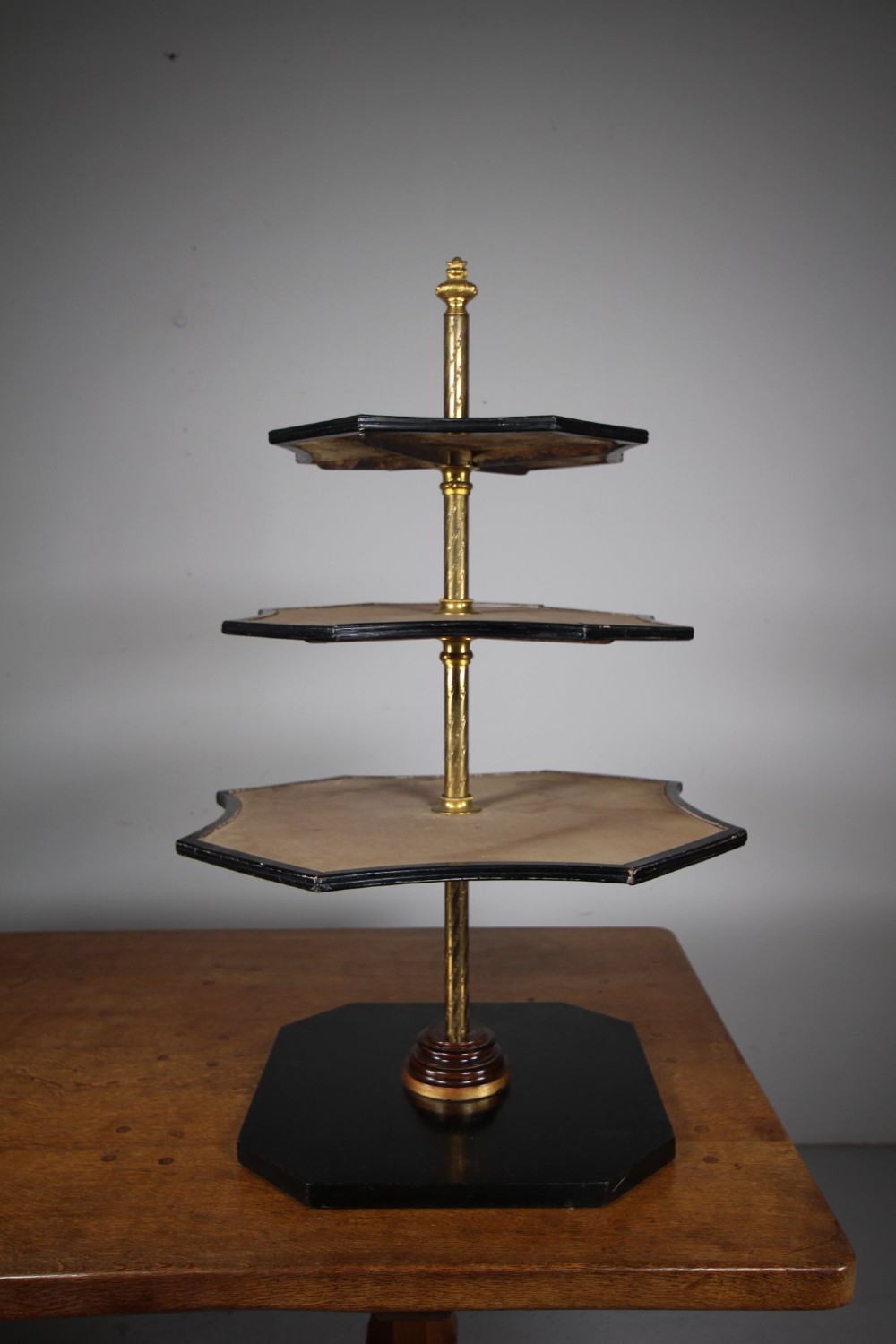 A nineteenth-century Victorian three-tiered shop display stand featuring a turned brass central column, shaped ebonised shelves, and a heavy black octagonal base. View II
