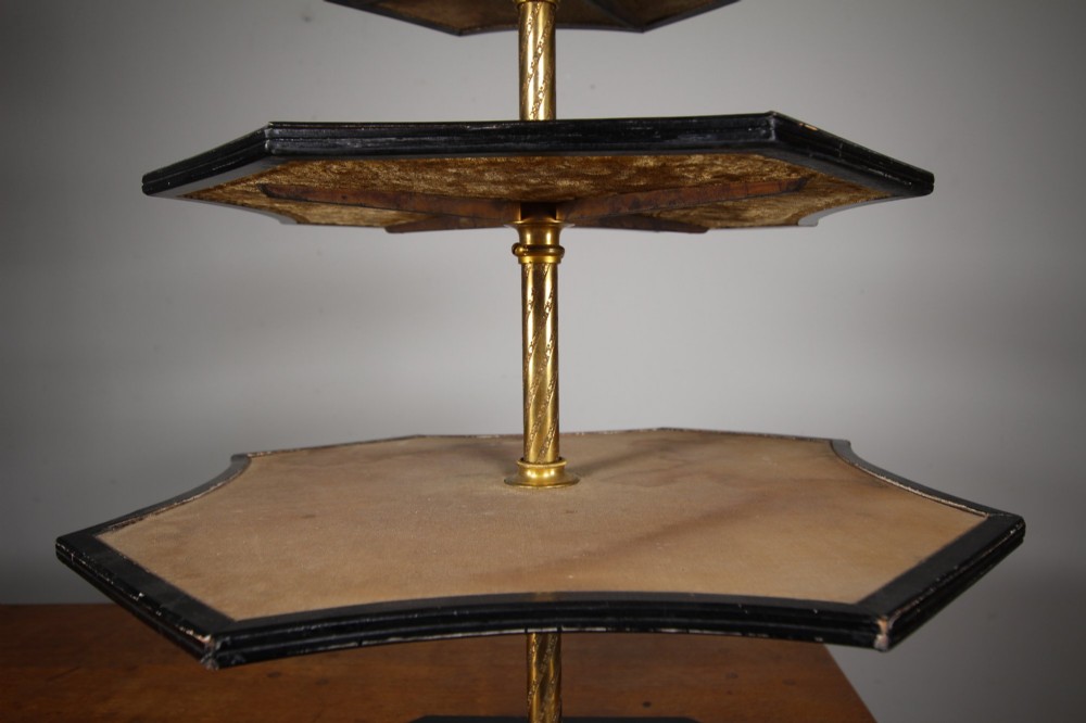 A nineteenth-century Victorian three-tiered shop display stand featuring a turned brass central column, shaped ebonised shelves, and a heavy black octagonal base. View IV