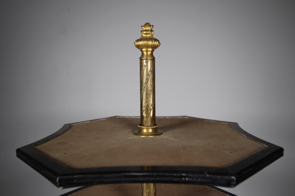 A nineteenth-century Victorian three-tiered shop display stand featuring a turned brass central column, shaped ebonised shelves, and a heavy black octagonal base. View VI
