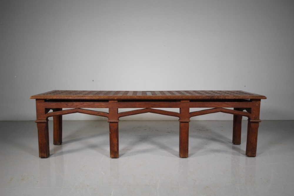 A long antique oak hall bench with a woven lattice top surface and pointed arch under-framing supported by square legs.
