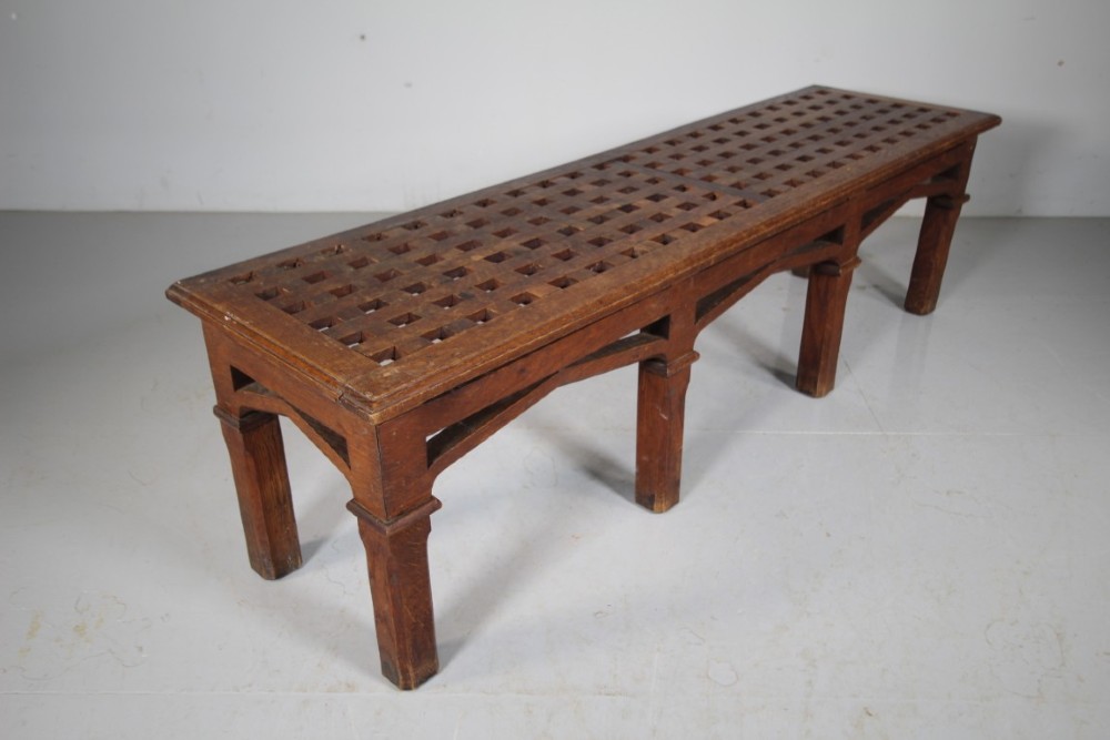 A long antique oak hall bench with a woven lattice top surface and pointed arch under-framing supported by square legs. View VI