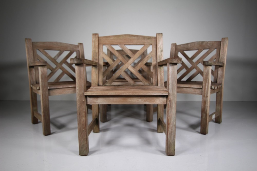A set of four weathered teak garden armchairs with geometric Chinese Chippendale lattice backrests and square legs.