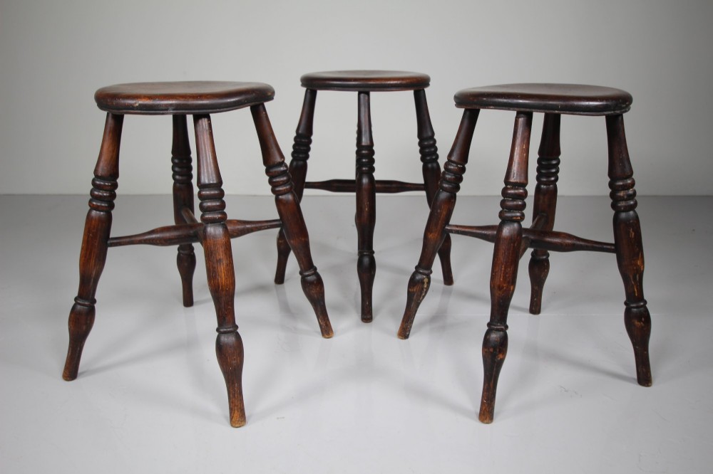 A set of three 19th-century dark brown wooden kitchen stools featuring circular seats and turned splayed legs with stretchers.