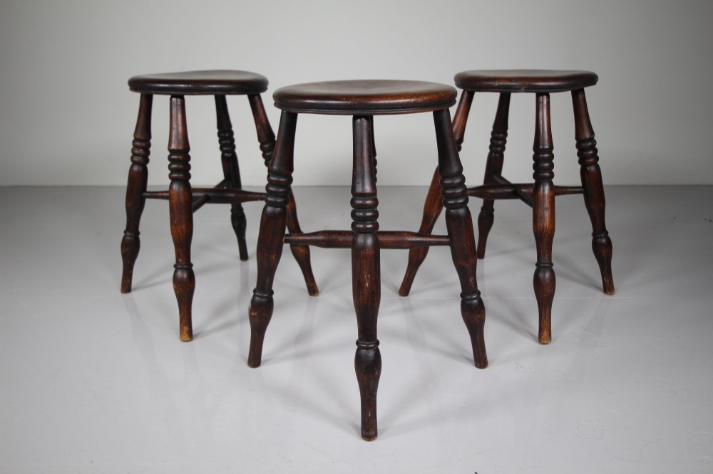 A set of three 19th-century dark brown wooden kitchen stools featuring circular seats and turned splayed legs with stretchers. View III