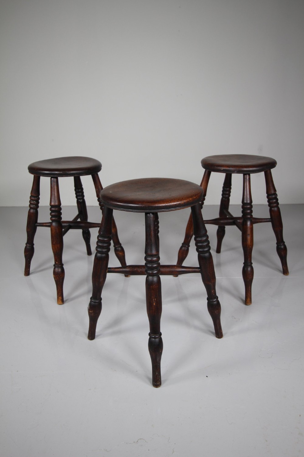 A set of three 19th-century dark brown wooden kitchen stools featuring circular seats and turned splayed legs with stretchers. View IV