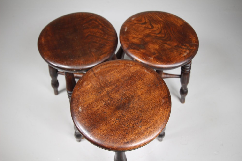 A set of three 19th-century dark brown wooden kitchen stools featuring circular seats and turned splayed legs with stretchers. View VI