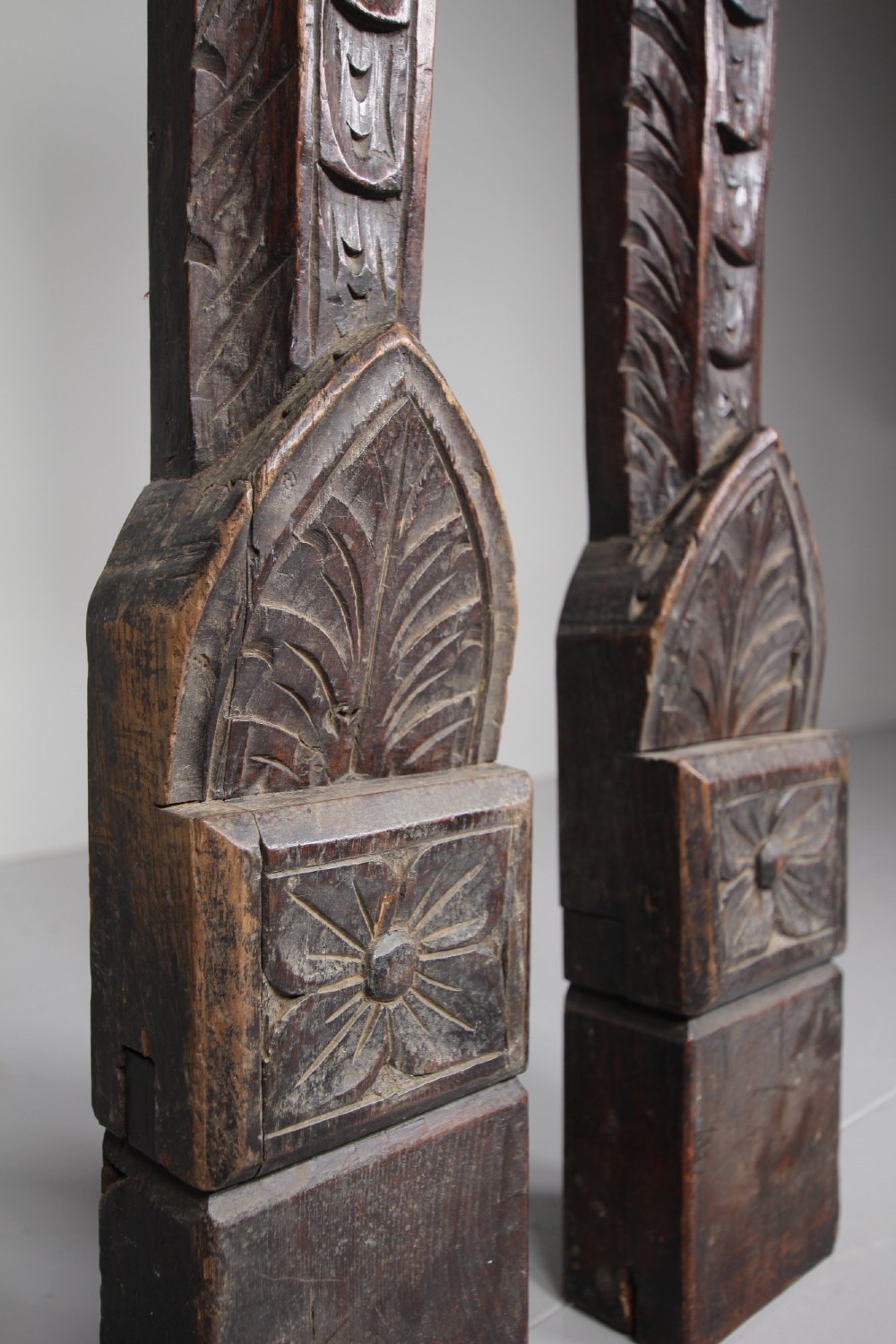 A pair of vertical hand-carved dark oak pilasters featuring stylized human figures at the top above foliage and geometric carved motifs. View IV