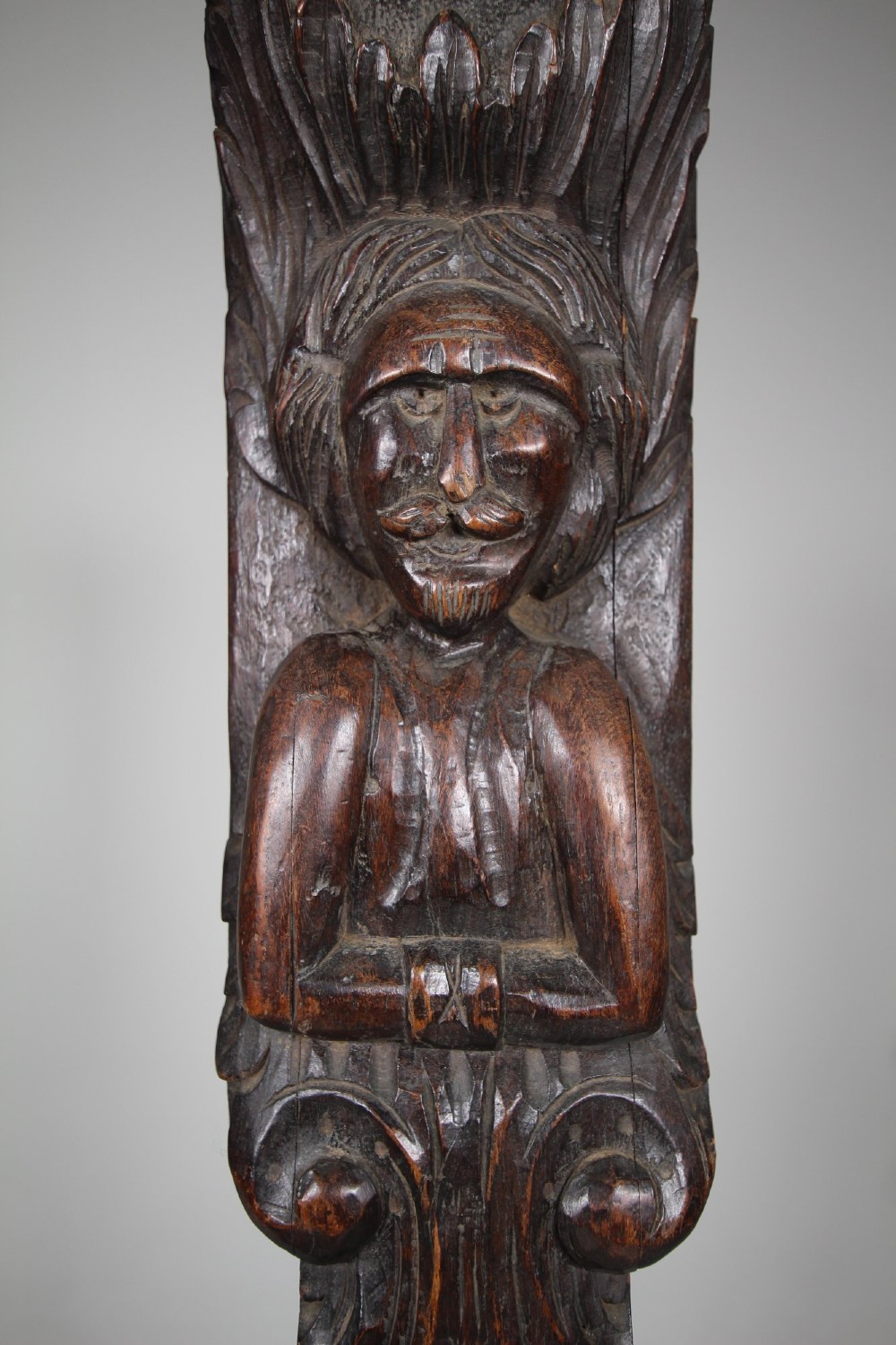 A pair of vertical hand-carved dark oak pilasters featuring stylized human figures at the top above foliage and geometric carved motifs. View IX