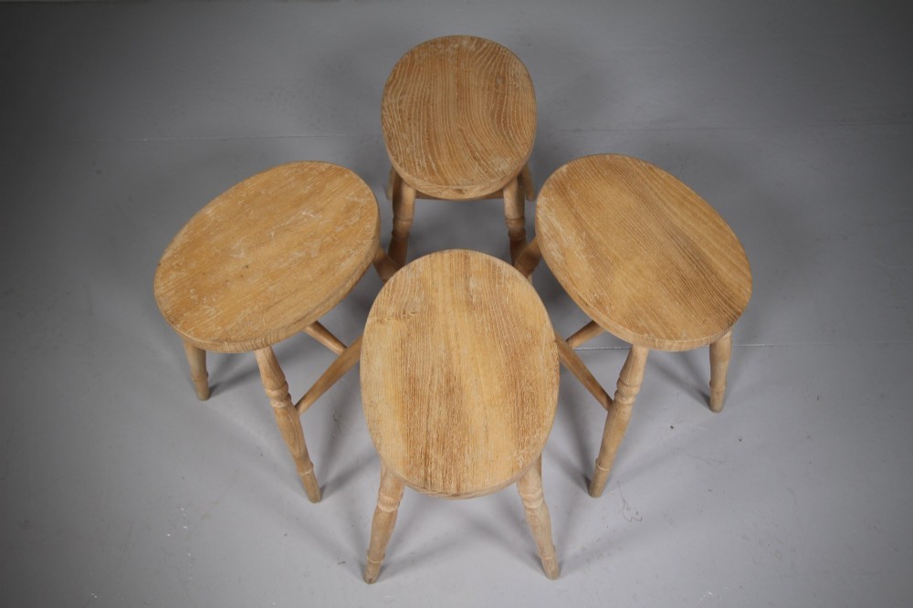 A set of four Edwardian natural wood dining stools featuring oval seats, turned legs, and lower stretchers. View V