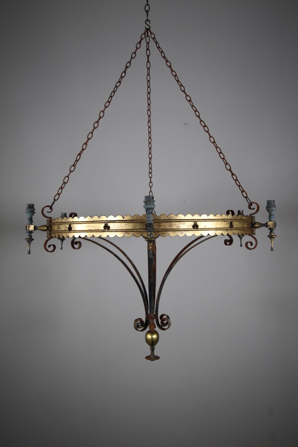 A 19th-century Gothic Revival brass and iron chandelier featuring a scalloped coronet band supported by suspension chains and curved lower scrollwork.