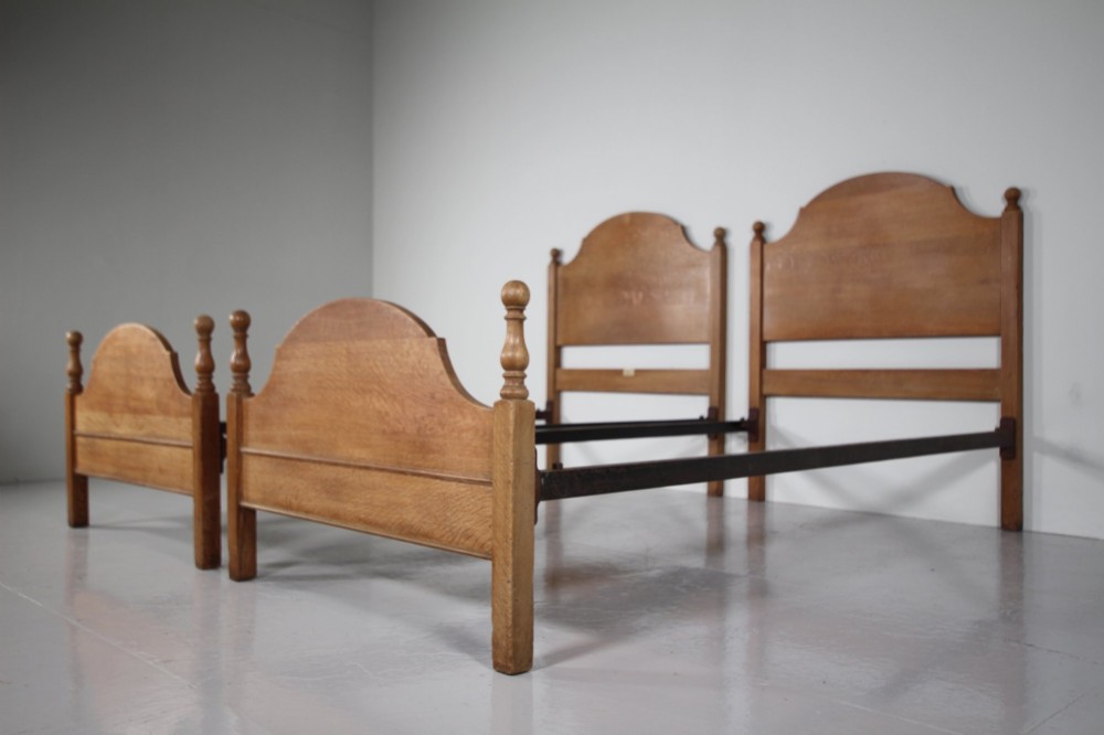 A matching pair of Edwardian oak single bed frames with gentle arched headboards, simple footboards, and turned corner posts.