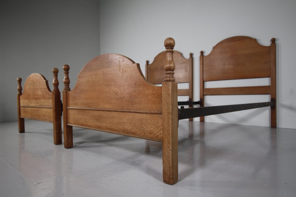 A matching pair of Edwardian oak single bed frames with gentle arched headboards, simple footboards, and turned corner posts. View V