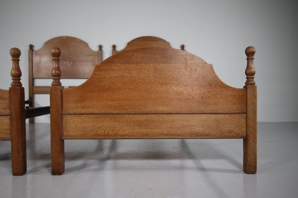 A matching pair of Edwardian oak single bed frames with gentle arched headboards, simple footboards, and turned corner posts. View VI