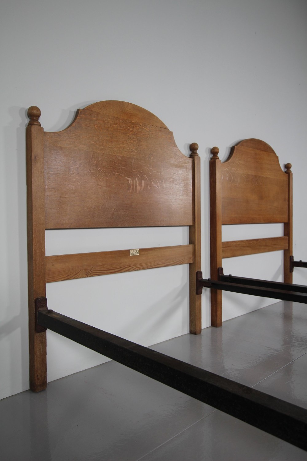 A matching pair of Edwardian oak single bed frames with gentle arched headboards, simple footboards, and turned corner posts. View VII