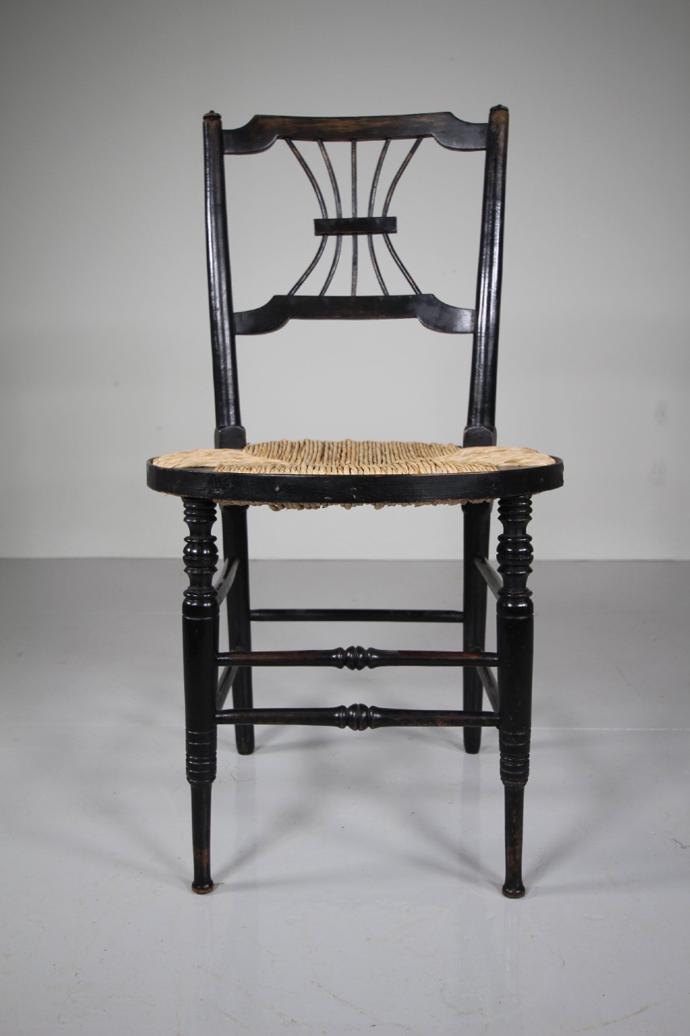 An ebonised wooden side chair with a woven rush seat, turned legs, and an intricate Rossetti splat back. View II