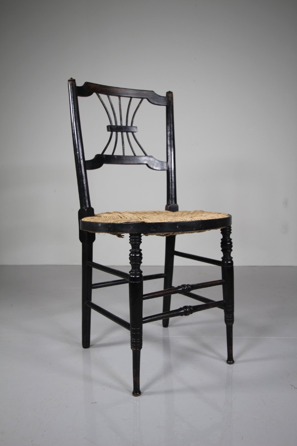An ebonised wooden side chair with a woven rush seat, turned legs, and an intricate Rossetti splat back. View IV