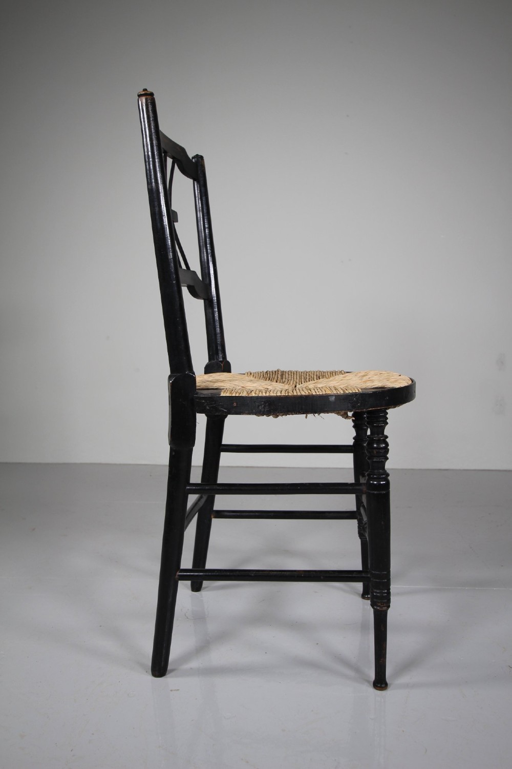 An ebonised wooden side chair with a woven rush seat, turned legs, and an intricate Rossetti splat back. View V