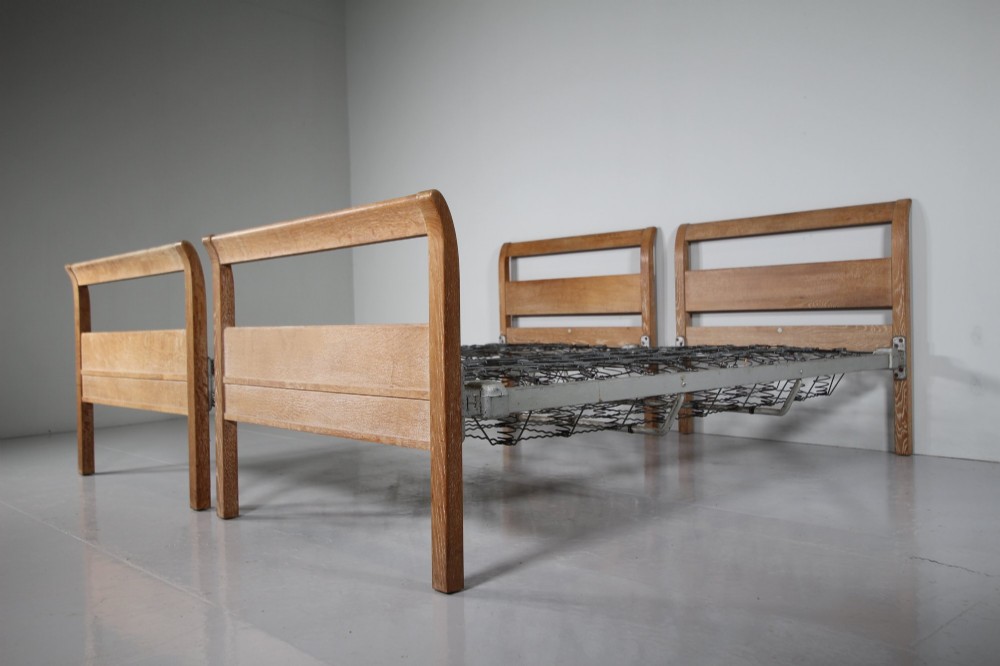 A pair of 1920s light oak single bed frames featuring curved headboards and metal spring mesh bases.