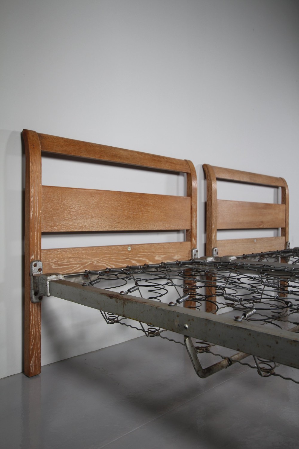 A pair of 1920s light oak single bed frames featuring curved headboards and metal spring mesh bases. View II