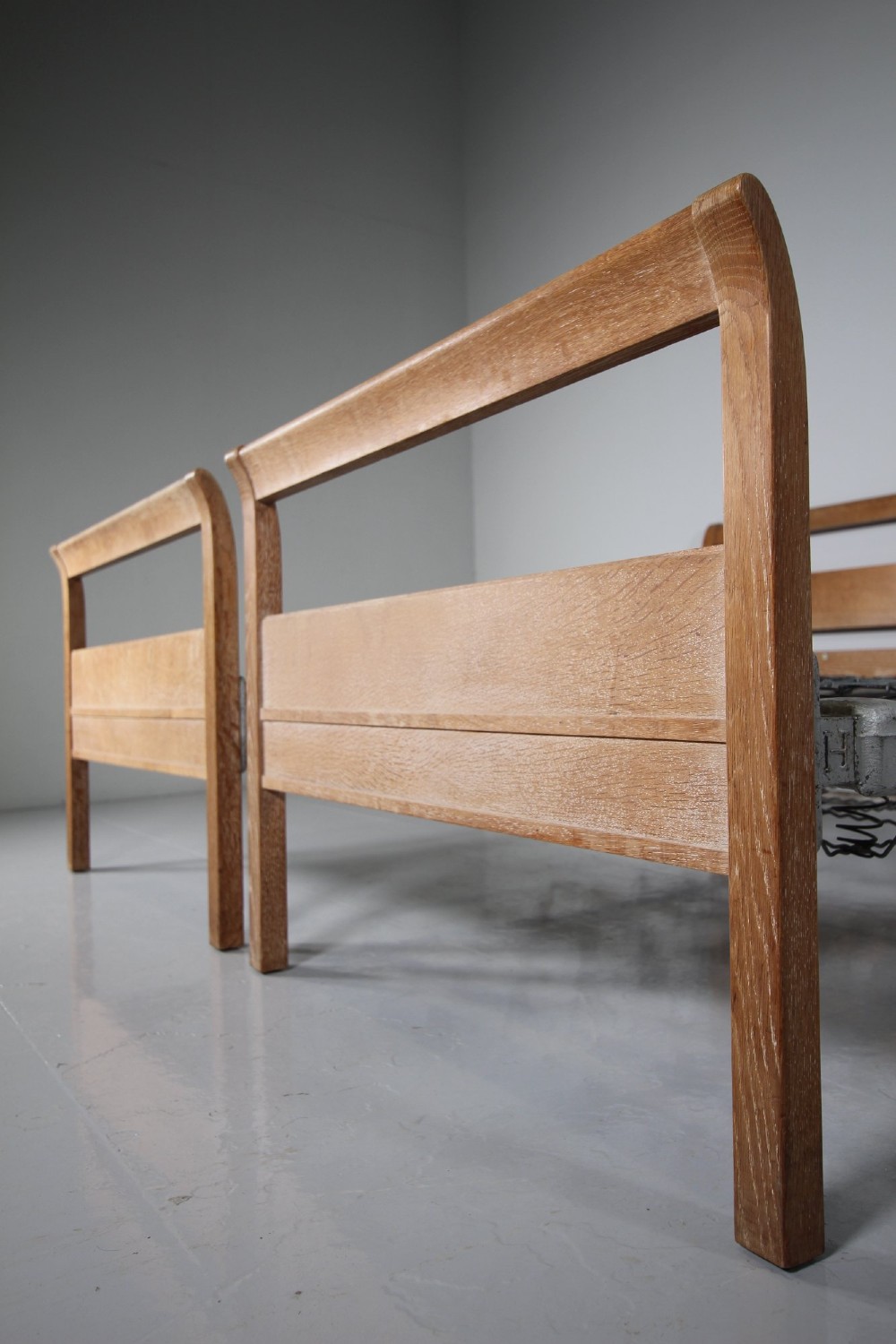 A pair of 1920s light oak single bed frames featuring curved headboards and metal spring mesh bases. View VII