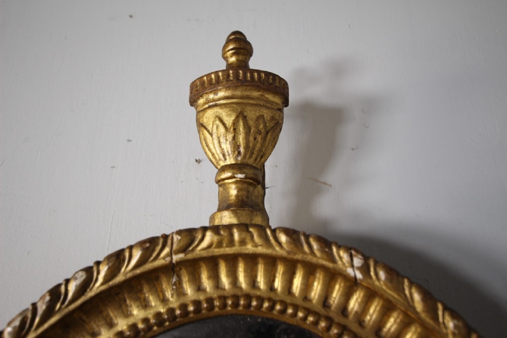 An 18th-century Neoclassical oval giltwood wall mirror featuring an urn finial top and fluted border along the carved frame. View III