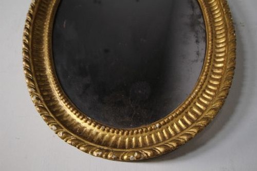 An 18th-century Neoclassical oval giltwood wall mirror featuring an urn finial top and fluted border along the carved frame. View V