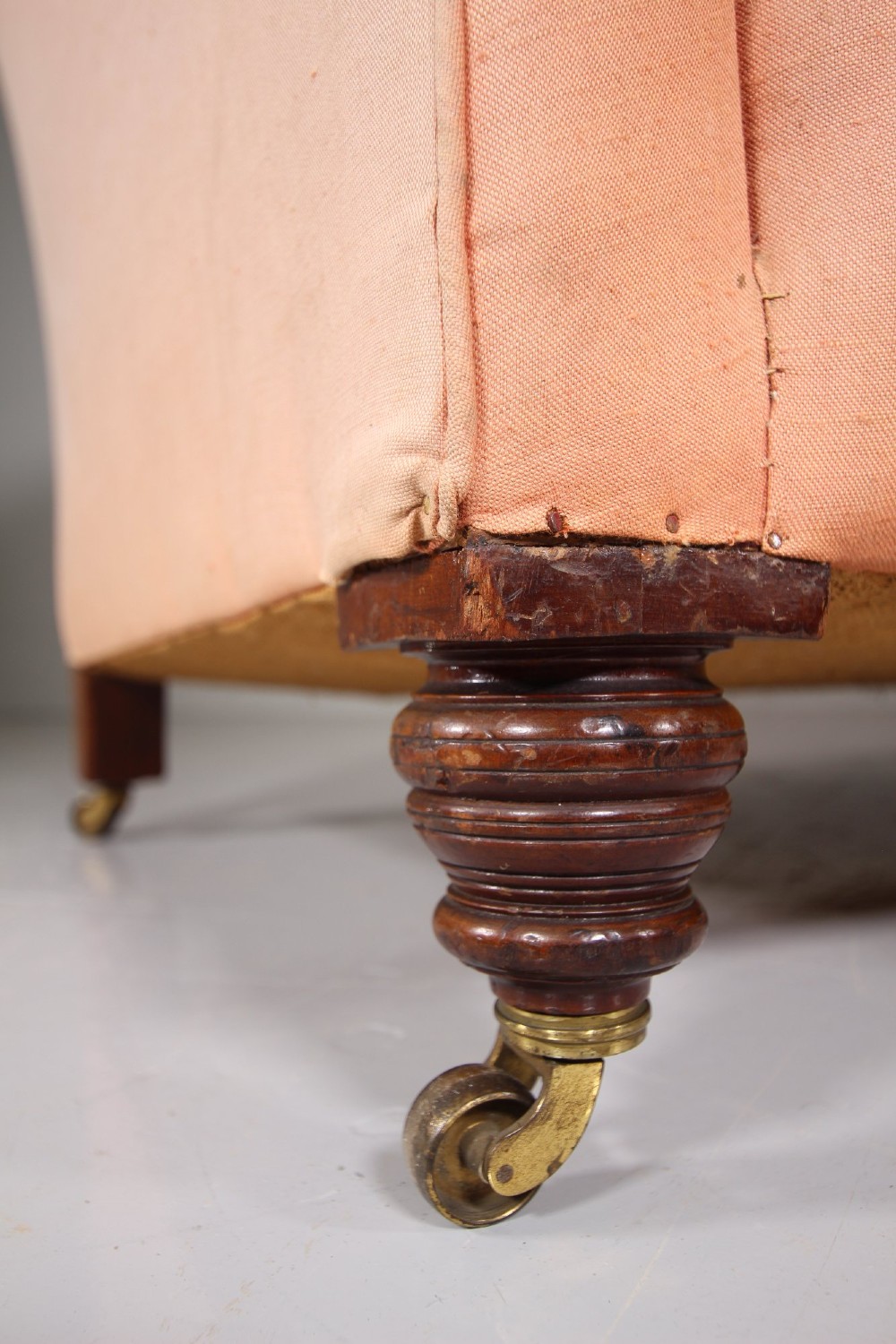A nineteenth-century two-seat sofa upholstered in peach-coloured fabric with a floral damask inner back panel, supported by turned mahogany legs on brass castors. View V