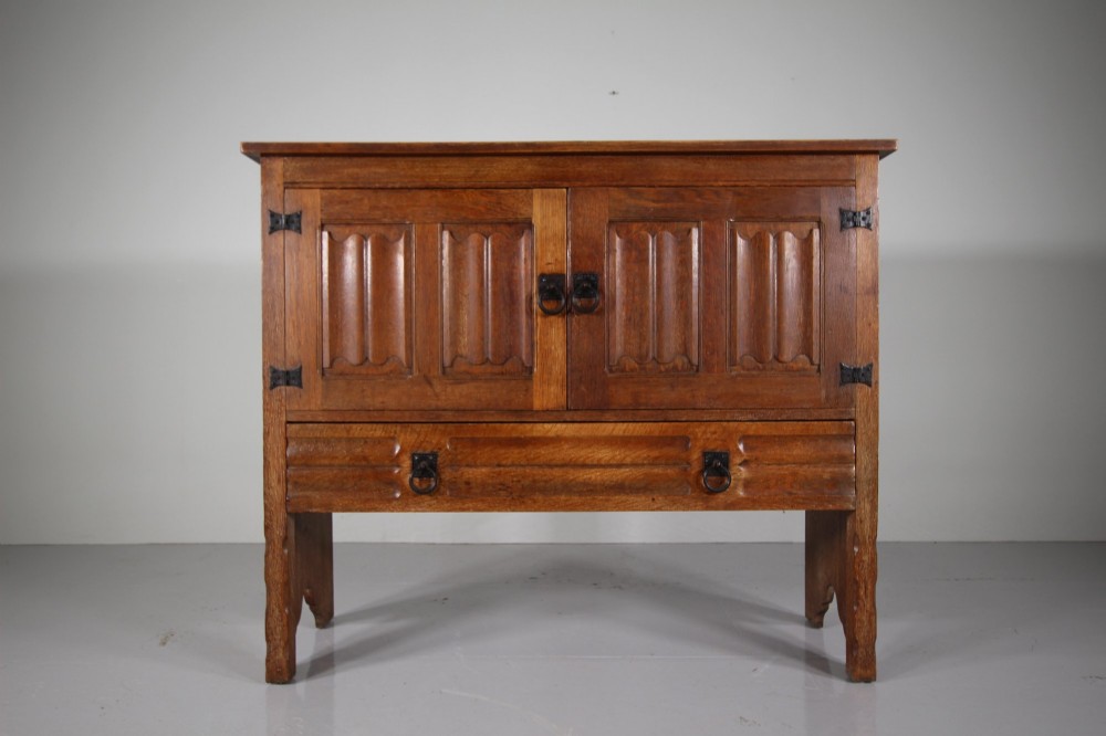 A 19th-century oak dresser base featuring two carved linenfold panel doors, iron drop handles, a single lower drawer, and carved plank supports. View IV