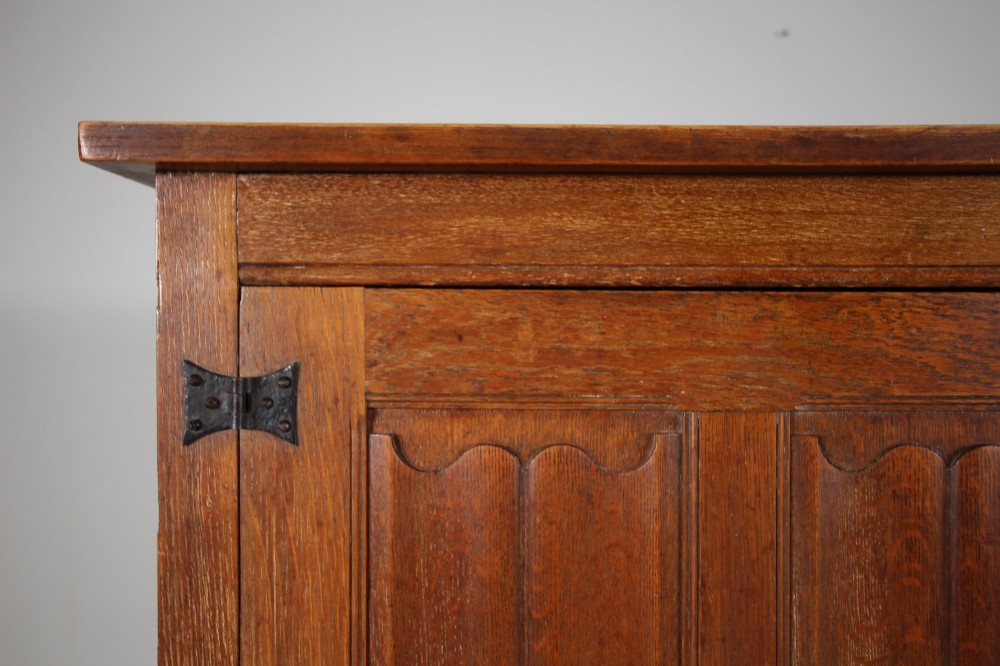 A 19th-century oak dresser base featuring two carved linenfold panel doors, iron drop handles, a single lower drawer, and carved plank supports. View V
