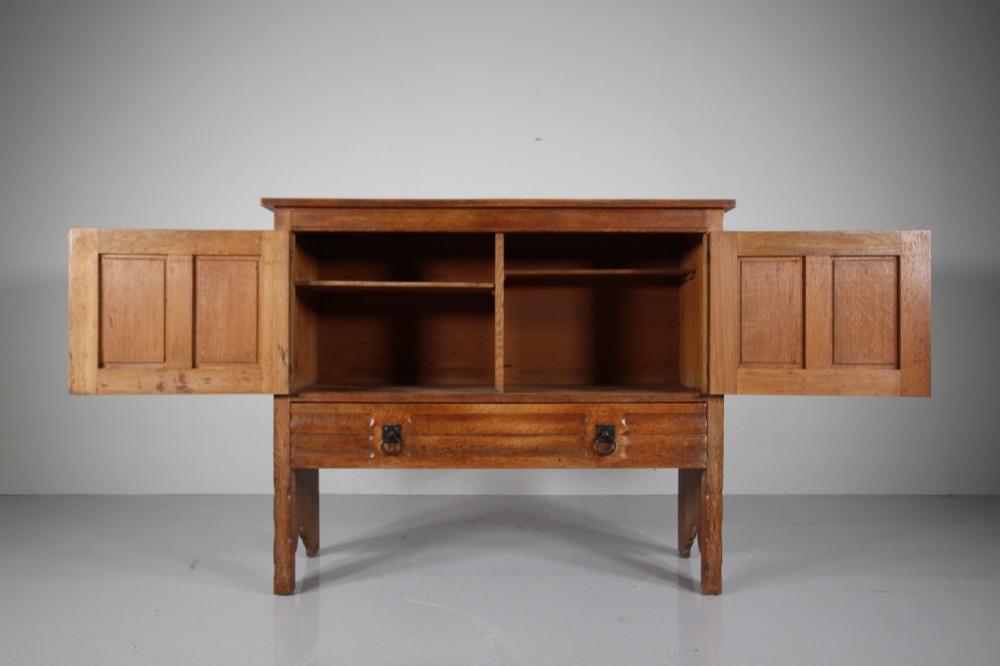A 19th-century oak dresser base featuring two carved linenfold panel doors, iron drop handles, a single lower drawer, and carved plank supports. View VI