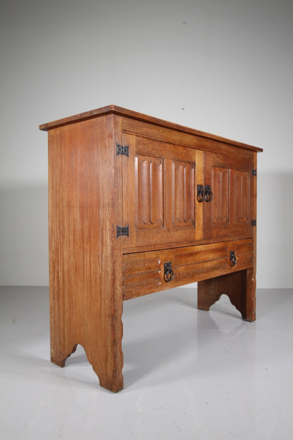 A 19th-century oak dresser base featuring two carved linenfold panel doors, iron drop handles, a single lower drawer, and carved plank supports. View VII