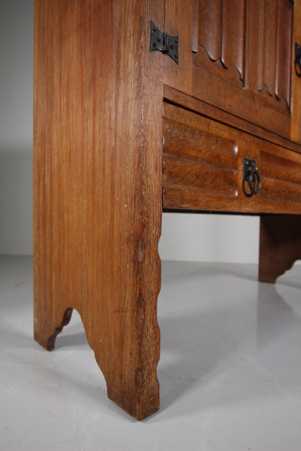A 19th-century oak dresser base featuring two carved linenfold panel doors, iron drop handles, a single lower drawer, and carved plank supports. View IX