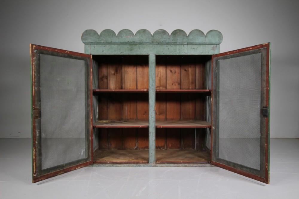 A large Georgian pine food safe in distressed sage green paint featuring a scalloped top pediment and wire mesh double doors. View II